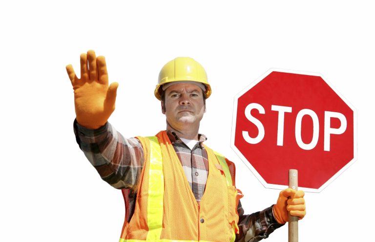 Mann in Sicherheitskleidung hält ein Stoppschild und zeigt mit der Hand auf Halt.