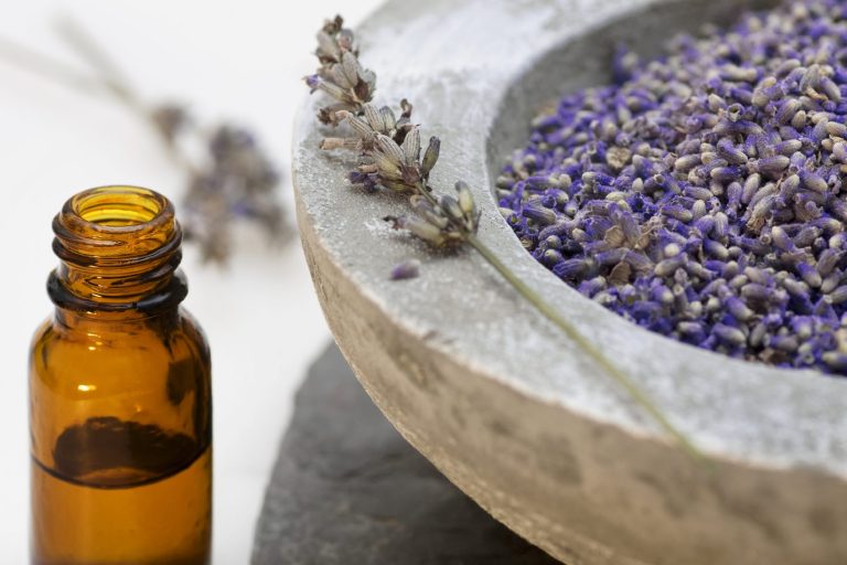 Braune Flasche mit ätherischem Öl neben einer Schale mit getrocknetem Lavendel.