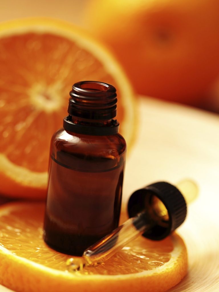 Braunes Fläschchen mit Pipette auf Orangenstücken, umgeben von orangefarbenem Hintergrund.