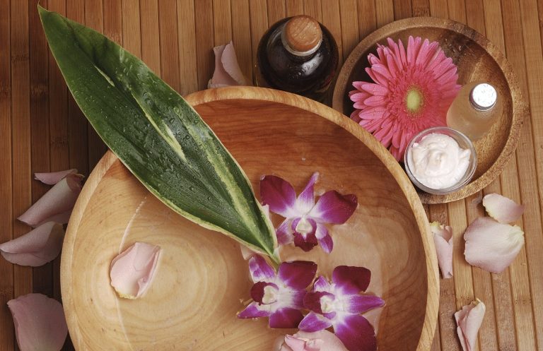 Holzschale mit Orchideenblüten, Blütenblättern und Wellnessprodukten.